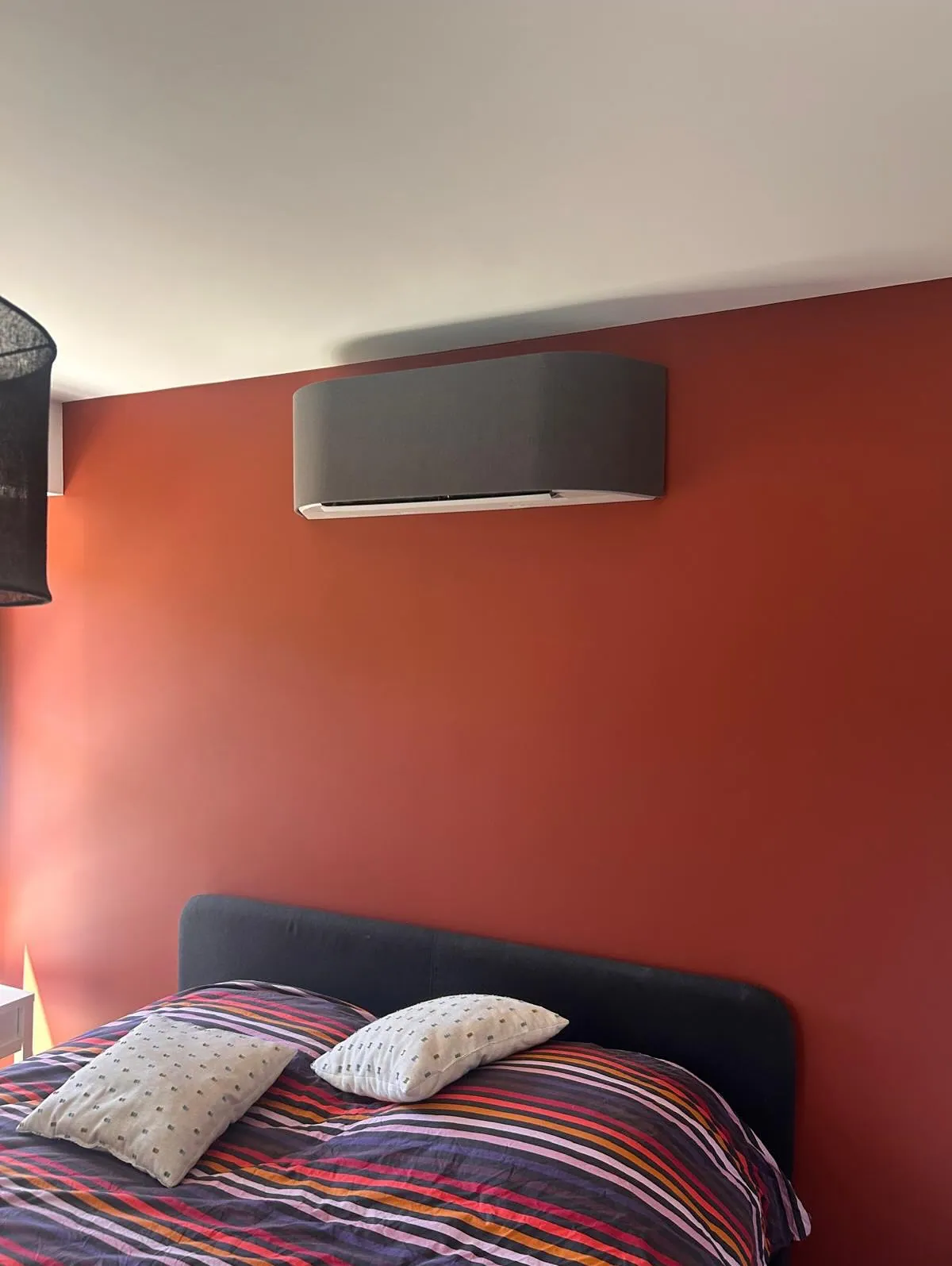 Climatiseur mural gris au-dessus d'un lit, sur un mur rouge brique