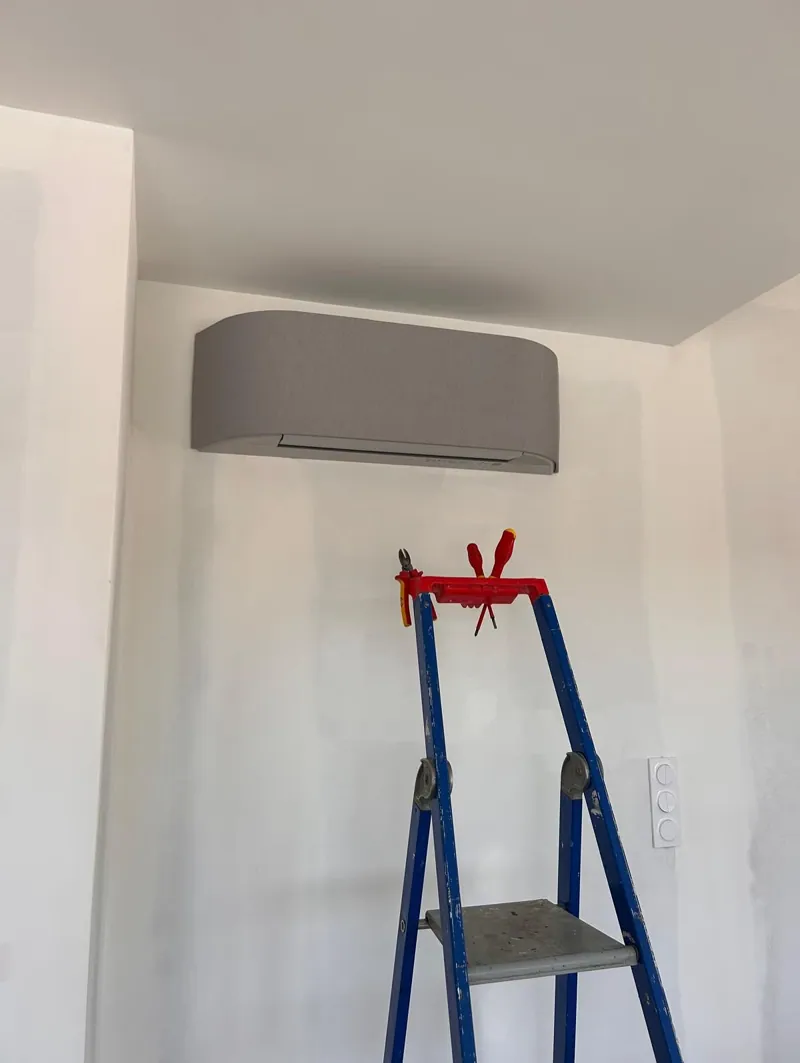 Climatiseur gris en cours de mise en service, escabeau au premier plan