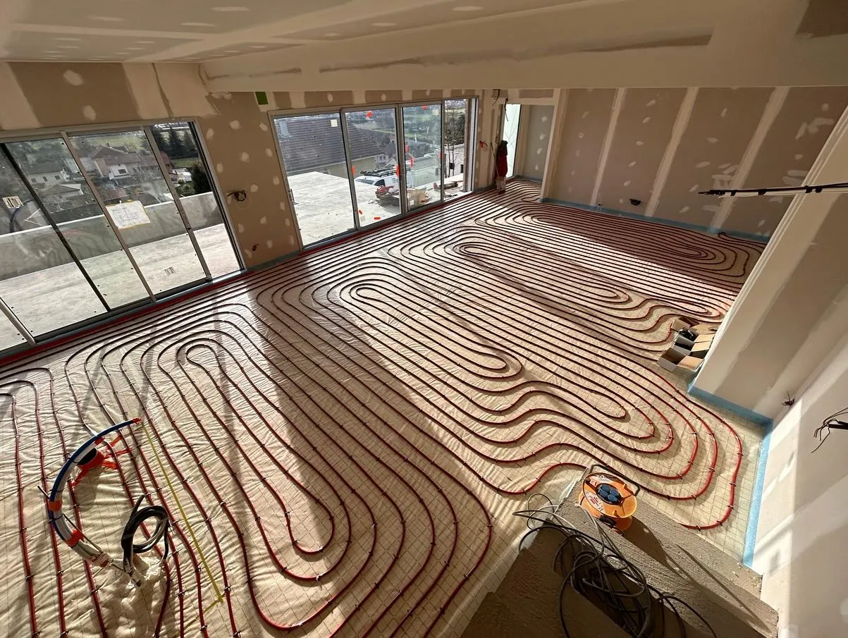 Plancher chauffant en cours de pose dans une grande pièce lumineuse, tubes rouges en serpentin